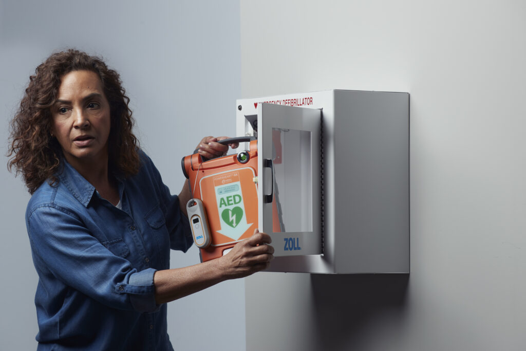 Woman pulling out a Powerheart G5 AED out of a wall cabinet