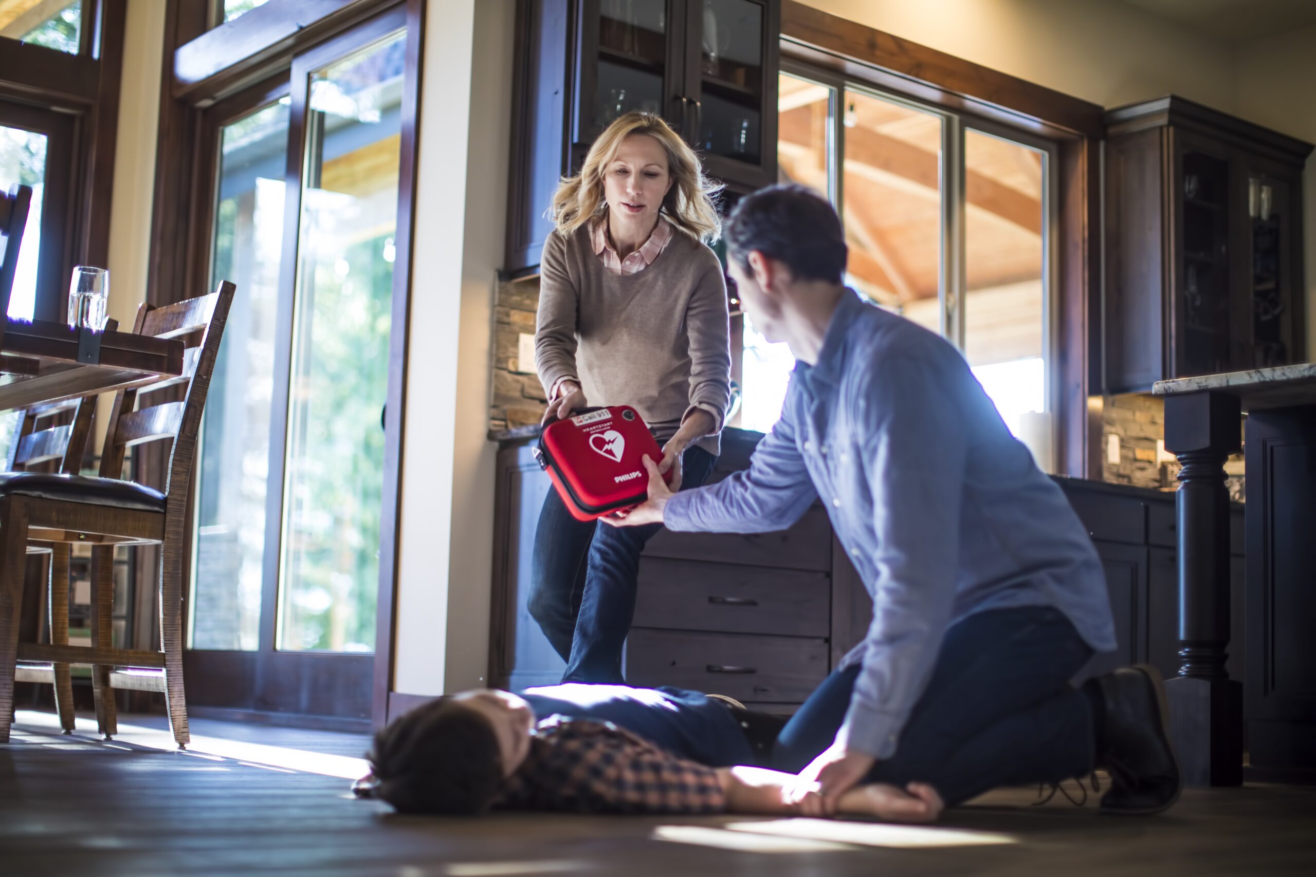 Woman bringing a Philips FRx AED to a man to resuscitate a child on the floor of a home